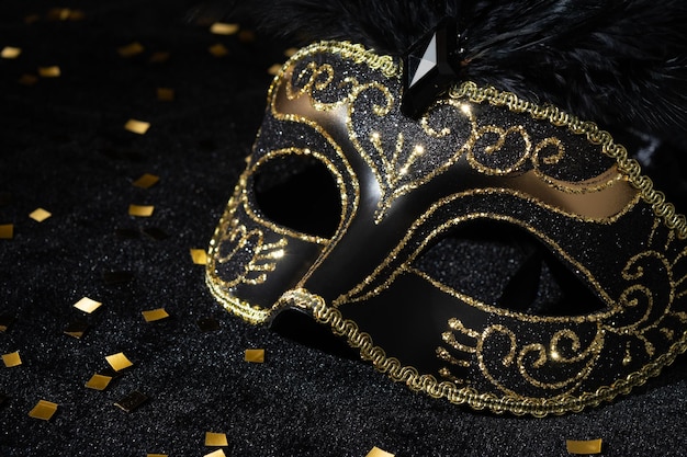 Closeup view of Masquerade gold mask with feathers and confetties on black background