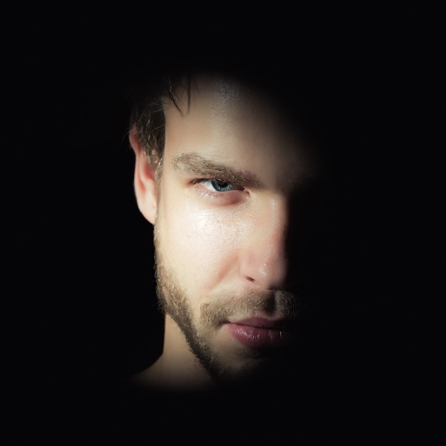 Closeup view portrait of one handsome bearded young macho man with strong look hazel eyes and sexy lips standing in light looking forward in studio on black background, square picture