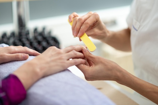 Closeup view of professional manicurist shaping the nails with a file