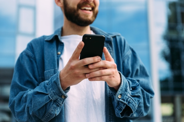 Closeup view of smartphone in hands of smiling bearded male hipster. Mobile technology concept.