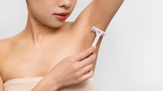 Closeup view of young asian lady shaving armpit with razor