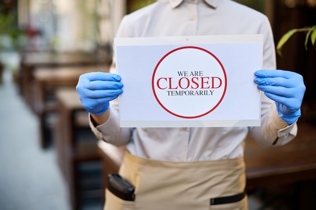 Closeup of waitress holding closed sign at outdoor cafe due to coronavirus epidemic