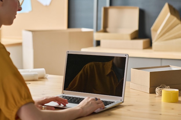 Closeup of warehouse worker sitting at table and doing online work on laptop