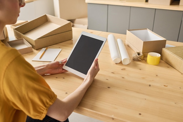 Closeup of warehouse worker sitting at table and using digital tablet to take online orders