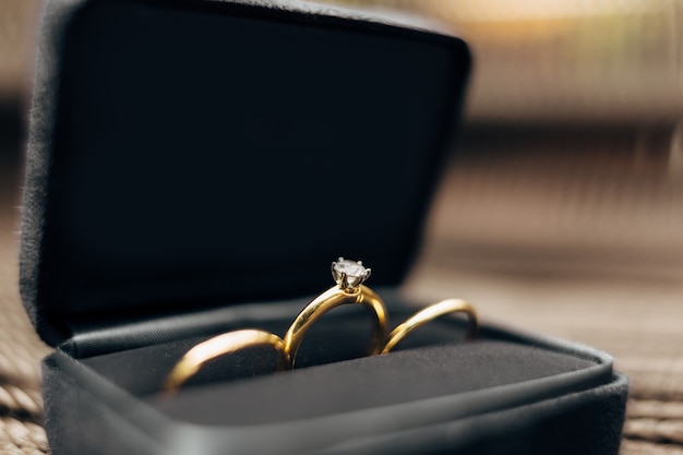 Closeup of wedding rings and an engagement ring with a large gem in a black velvet box against a