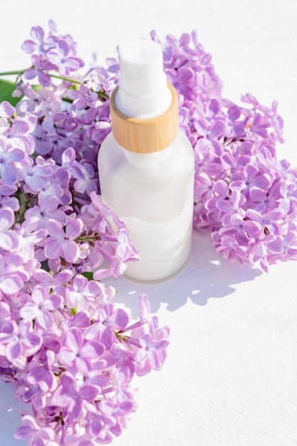 Closeup of a white bottle with natural cosmetic cream and a branch of lilac on a white background Cosmetic beauty concept