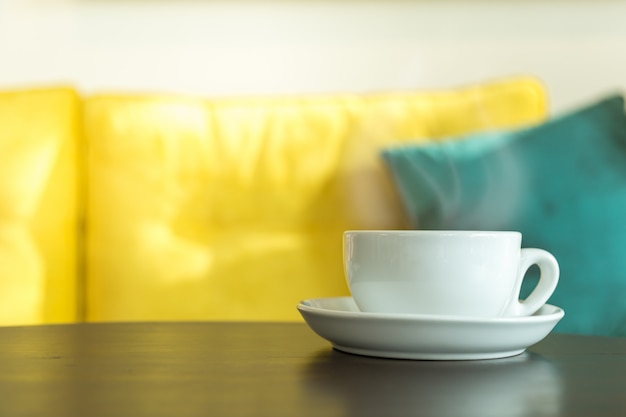 Closeup of white cup of hot coffee latte with milk foam on wooden table in morning sunlight in restaurant use for wallpaper or cover page concept.