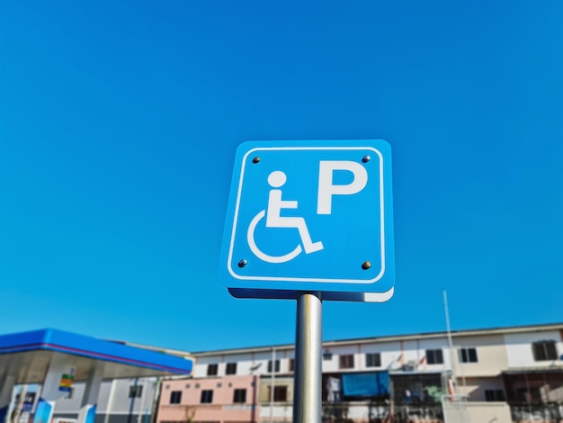 Closeup White Handicapped Parking Sign on Blue Label Against Clear Blue Sky