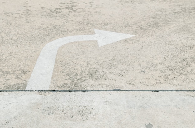 Photo closeup white painted arrow sign in right side on cement street floor textured background