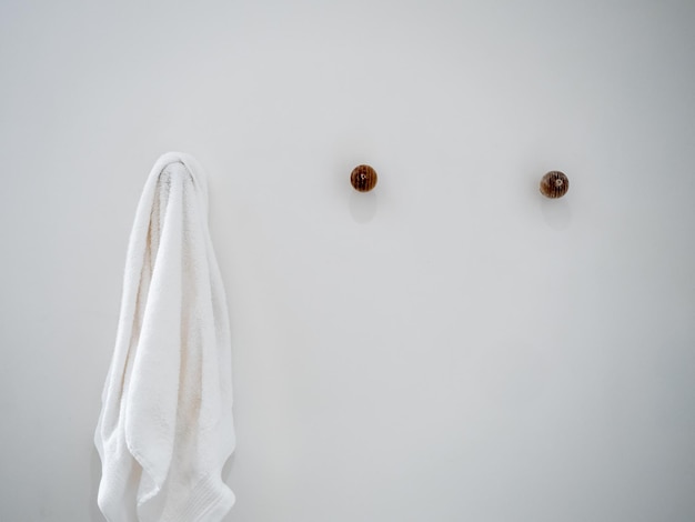 Closeup white towel hanging on a hook hanger on white wall background in a hotel room with copy space minimal style