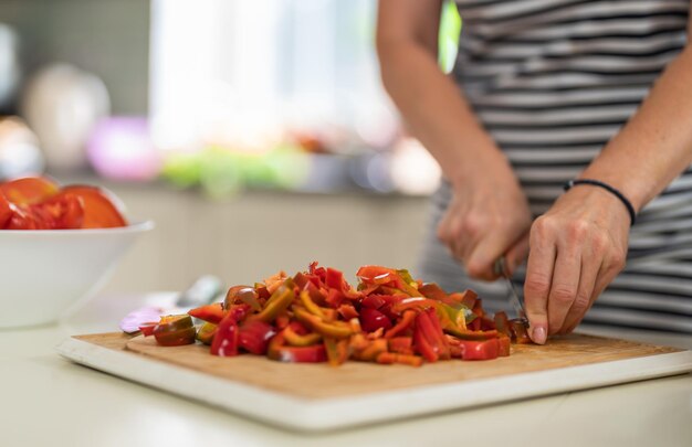 Photo closeup of a woman cutting bell pepper with a kitchen knife in a bright kitchen