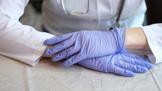 Closeup of woman doctor in medical gown putting hands on table posing in clinic office