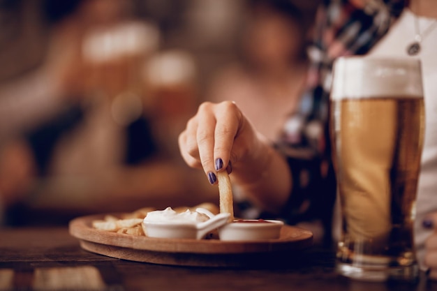 Closeup of woman eating French fries and drinking beer in a tavern