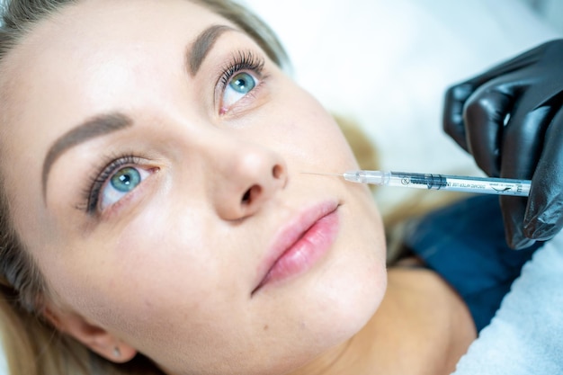 Closeup of woman face and hand in surgical glove holding syringe near her lips ready to receive beau