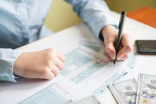 Closeup of a woman filling out a 1040 form while sitting at a table Tax concept financial document