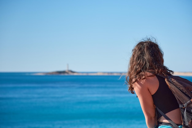 A closeup of a woman from behind looking at the Trafalgar lighthouse in the distance