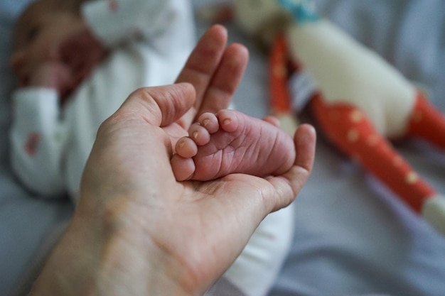 Photo closeup of woman gently stroking with hand tiny leg of her newborn baby with perfect skin top view