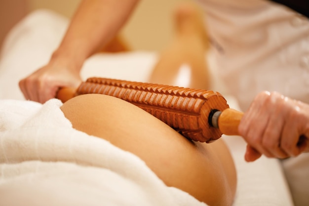 Closeup of woman getting buttocks massage with wooden rolling pin during maderotherapy at the spa