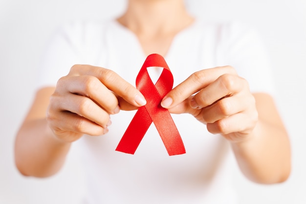 Closeup woman hand holding red ribbon HIV, world AIDS day awareness ribbon. Healthcare and medicine concept.