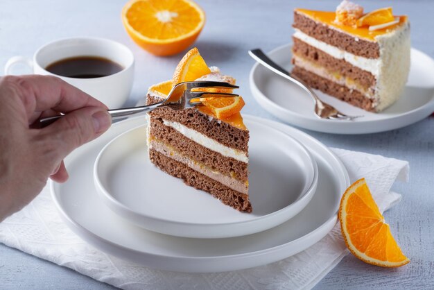 Closeup woman hand using stainless fork to eating delicious orange cake on table in cafe