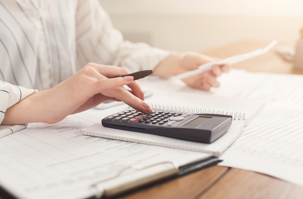 Closeup of woman hands counting on calculator and holding bills. Financial background, count and pay an account, copy space, selective focus