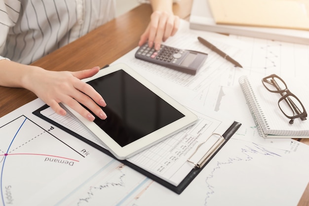 Closeup of woman hands counting on calculator and using digital tablet with blank screen for advertisement. Financial background, count and pay an account, copy space