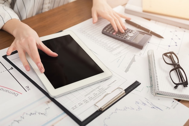 Closeup of woman hands counting on calculator and using digital tablet with blank screen for advertisement. Financial background, count and pay an account, copy space