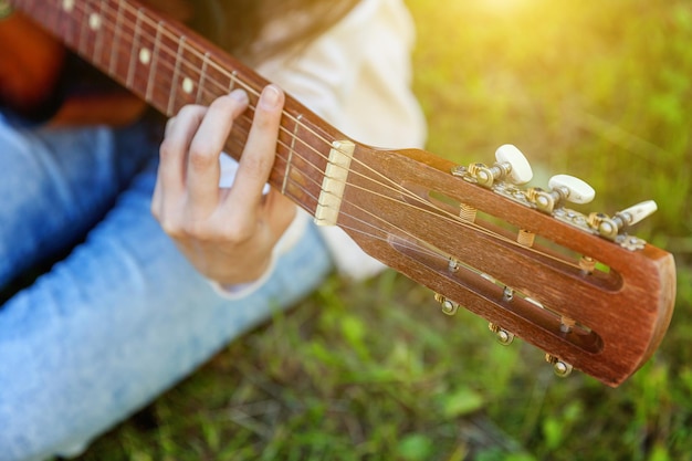 Closeup of woman hands playing acoustic guitar on park or garden background. Teen girl learning to play song and writing music. Hobby, lifestyle, relax, Instrument, leisure, education concept