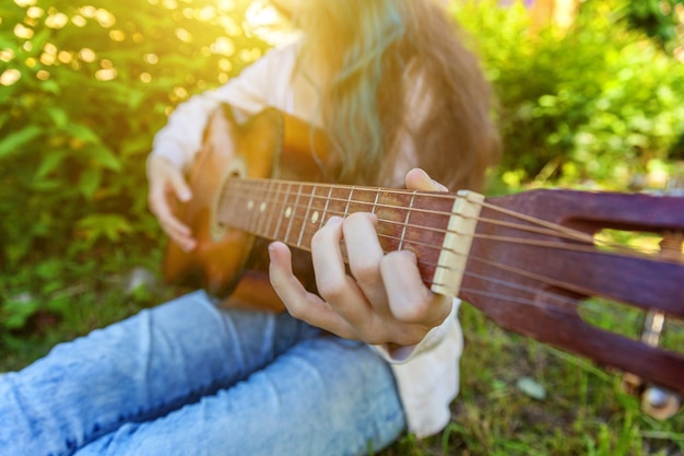 Closeup of woman hands playing acoustic guitar on park or garden background Teen girl learning to play song and writing music