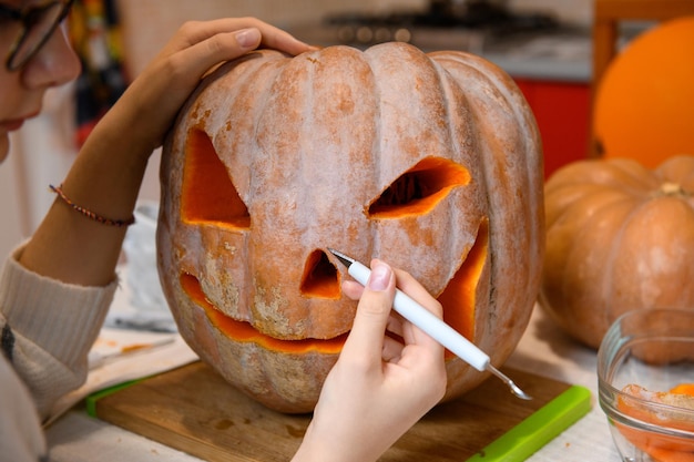 Closeup on woman hands using knife to carve big orange pumpkin JackOLantern for Halloween party