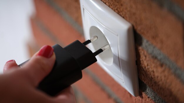 Closeup of woman holding hand and inserting plug into socket power line with switches and