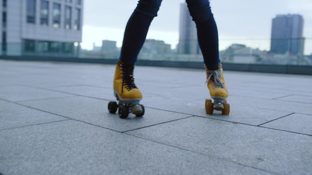 Closeup woman legs riding on roller skates outdoor Sporty red hair girl performing element of roller skating on city street Active roller skater training in yellow rollerblades outside