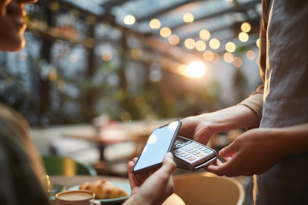 Photo closeup woman paying via smartphone in cafe