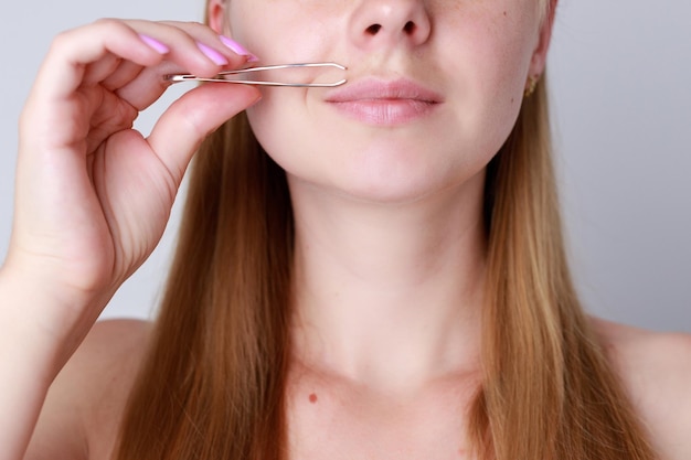 Closeup woman plucks facial hair with tweezers smooth female face epilation