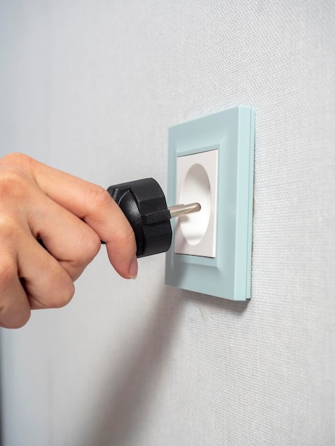 Closeup of a woman's hand holding a black plug and about to plug it into a blue outlet on the wall in the house The concept of the need for electricity in the house Side view