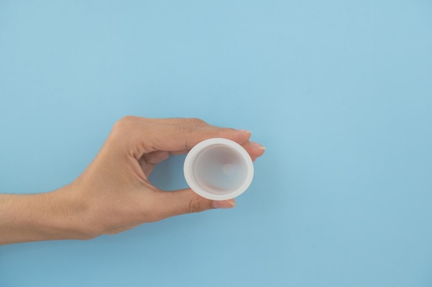 Closeup of a woman's hand holding a menstrual cup against a blue background