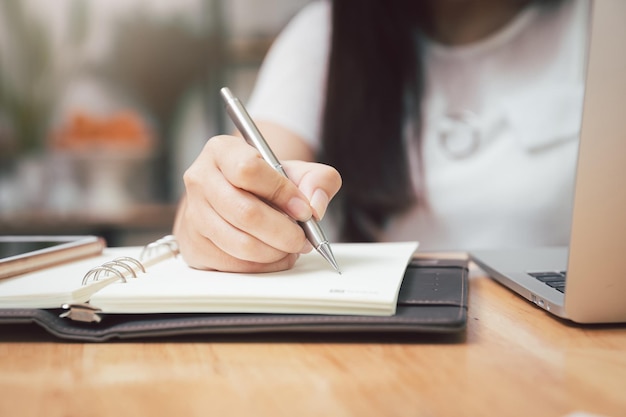 Closeup of woman's hand holding a pen on notebook Freelance journalist working at home