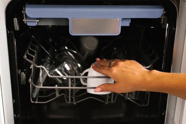 Closeup of a woman's hand loading dishes emptying or unloading them from an open automatic builtin