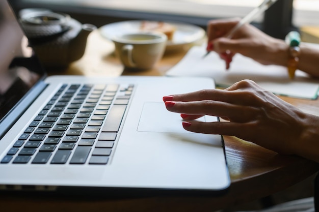 Closeup of a woman's hand working with a laptop in a coffee shop