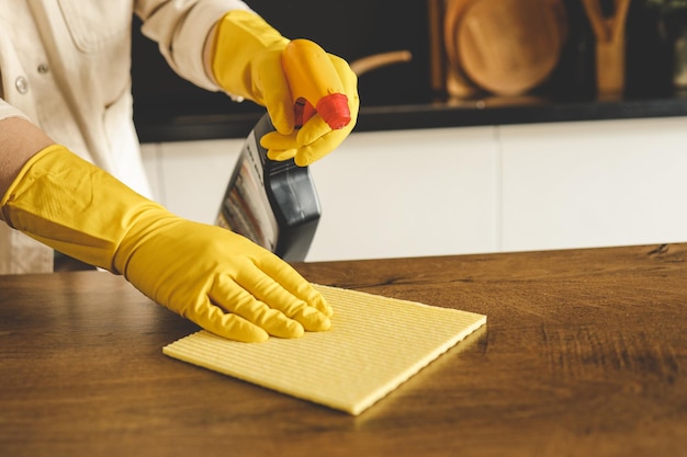 Closeup on woman's hands in yellow protective rubber gloves cleaning kitchen cabinets with sponge