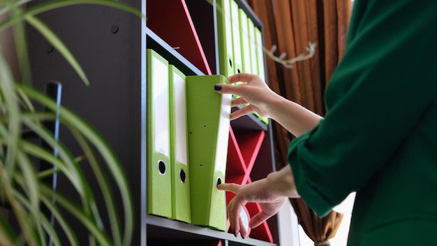 Closeup of woman taking of shelf green paper folder office work documentation and accounting