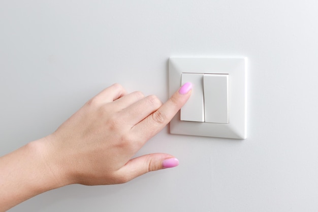 Closeup woman turns on the switch on the wall home light switch