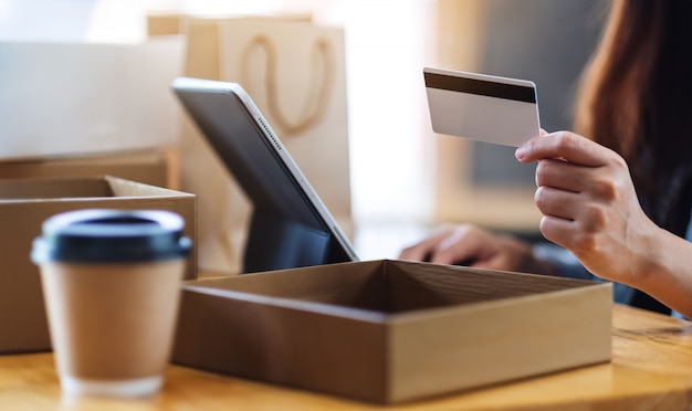 Closeup  of a woman using tablet pc and credit card for online shopping with postal parcel box and shopping bags on the table