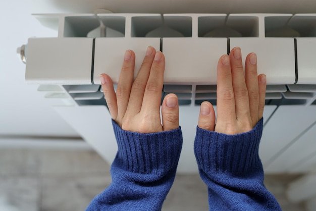 Closeup of woman warming her hands on the heater at home during cold winter days Heating season