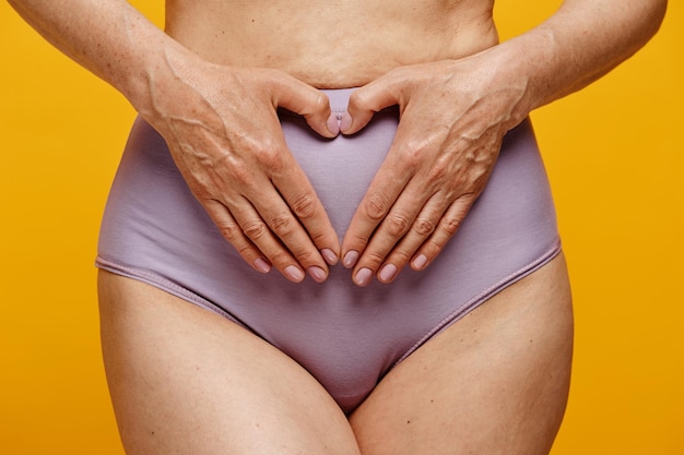 Closeup of woman wearing underwear holding hands gently on belly in uterus area