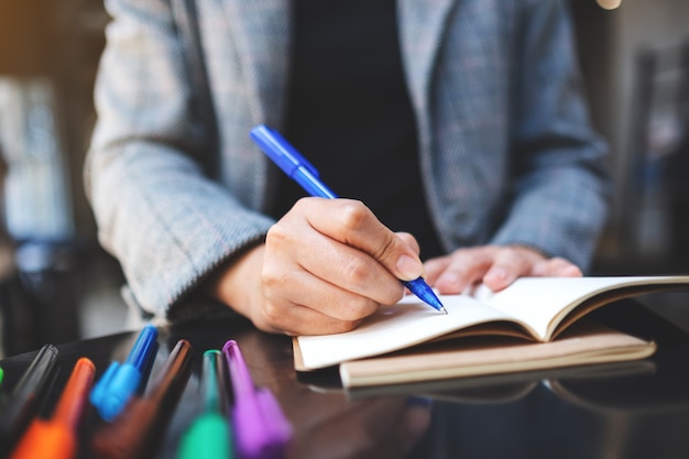 Closeup  of a woman writing on a blank notebook with colored pens on the table