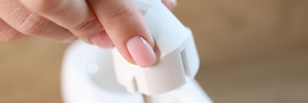 Closeup of womans hand inserting electric plug into socket connecting electrical devices