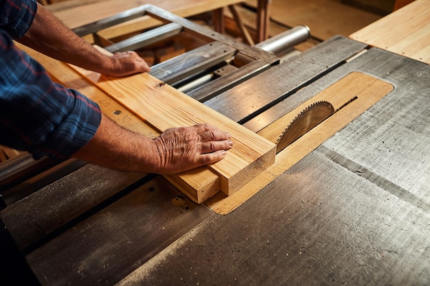 Closeup of wood cutting table with electric circular saw Senior Professional carpenter in uniform cutting wooden board at sawmill carpentry manufacturing Sawing machine