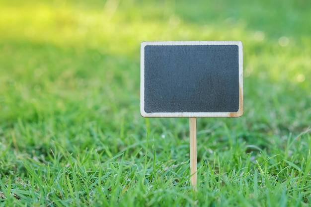 Closeup wooden black board in square shape on green grass in the park textured background