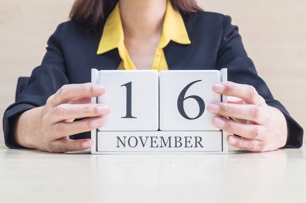 Closeup wooden calendar with black 16 november word on blurred working woman hand